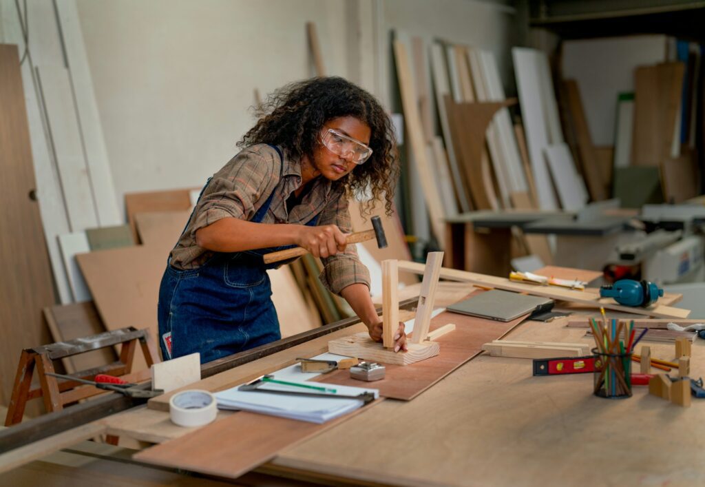 Asian wood worker or carpenter woman use hammer to set and produce wooden chair in workplace