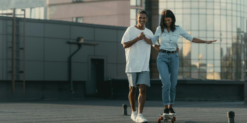 handsome-young-man-helping-his-girlfriend-to-ride-skateboard.jpg