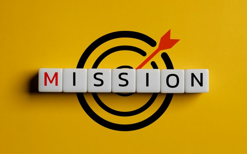 Wooden cubes with the word mission and icon target on a yellow background.